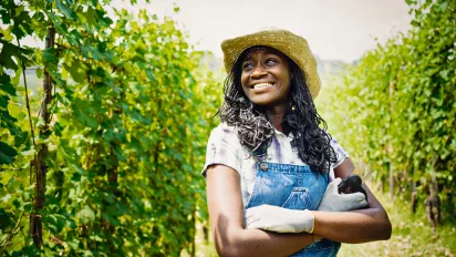 Girl with a hat standing in a field with green crops