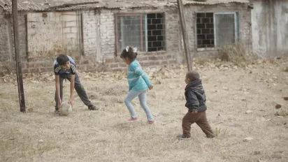 Tres niños juegan con una pelota en un patio humilde.