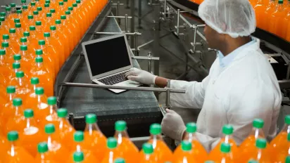 Male worker using laptop amidst production line in juice factory