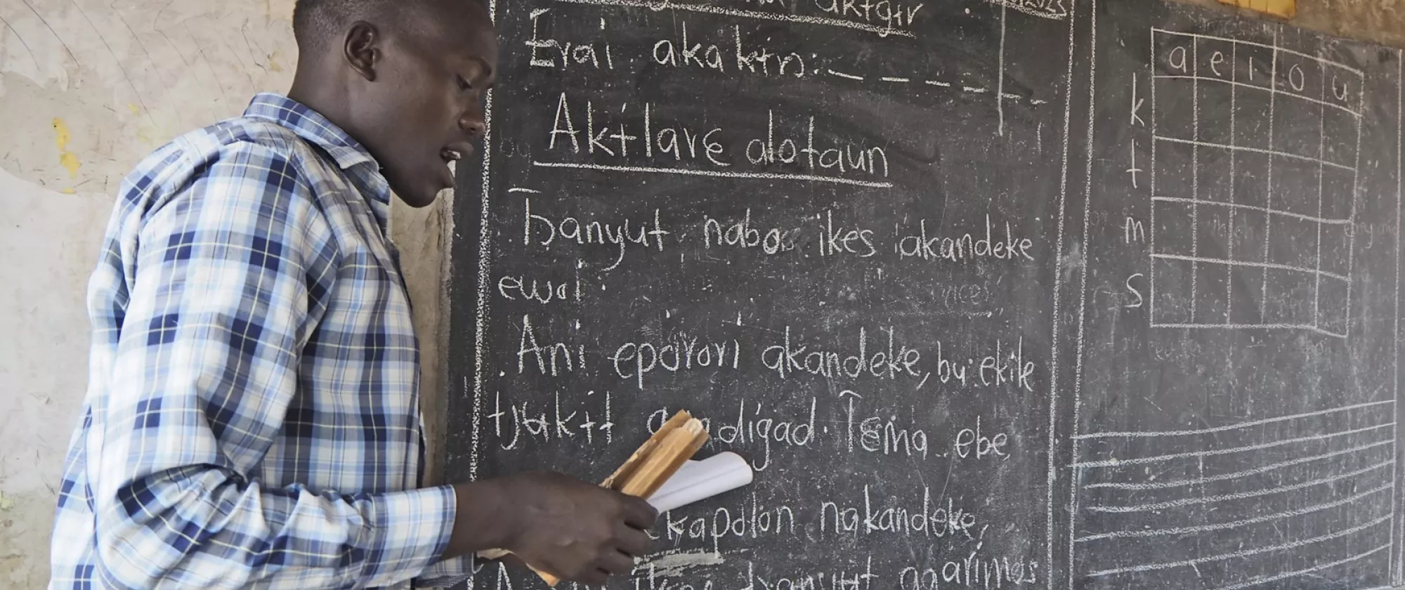 Teacher in checkered shirt in front of a blackboard