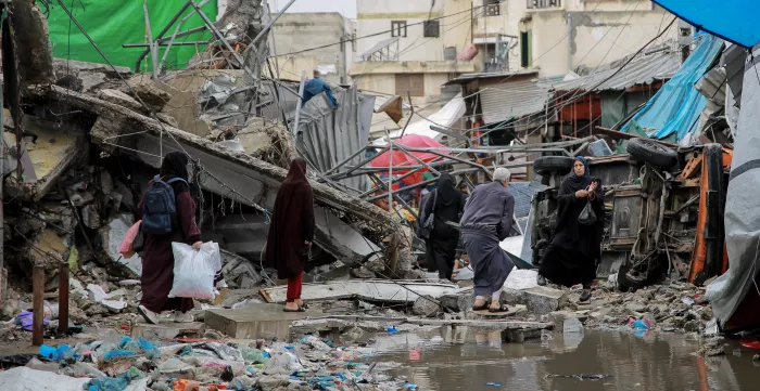 People crossing the road in front of a commercial shop destroyed during the war